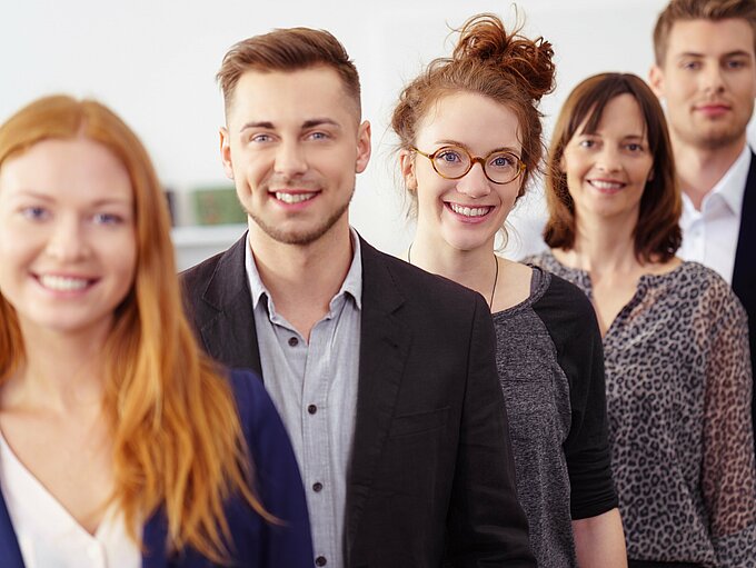 Auf dem Bild abgebildet sind fünf Studierende (drei Frauen und zwei Männer), die nebeneinander stehen und in die Kamera lächeln.