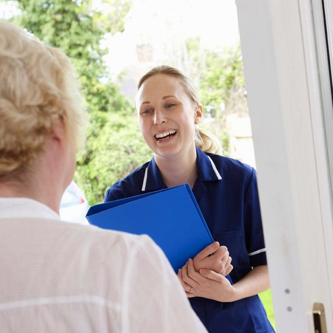 Auf dem Bild sieht man eine Pflegekraft, die ihre ältere Patientin zu Hause besucht.