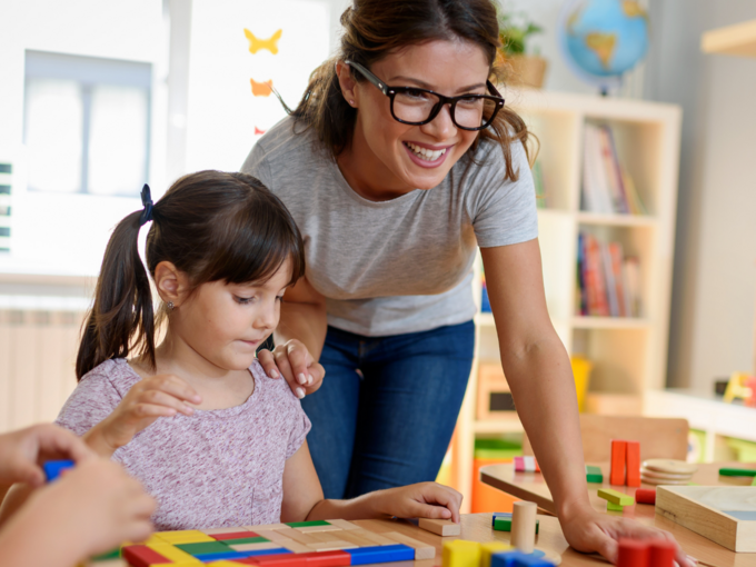 Abgebildet ist eine Erzieherin, die drei Kinder betreut.