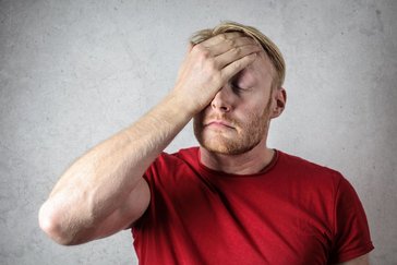 Ein Mann in einem roten T-Shirt bedeckt sein Gesicht mit seiner Hand.
