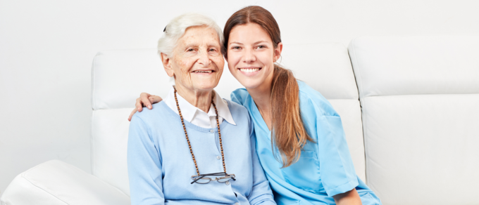 Abgebildet ist eine Pflegefachhelferin, die sich um eine ältere Dame kümmert.