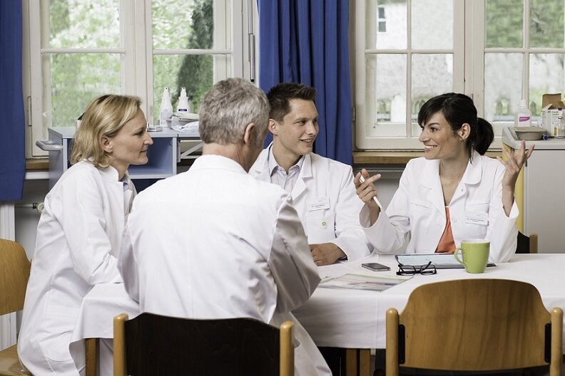 Auf dem Bild sind vier Kollegen abgebildet, die in einer Klinik zusammensitzen.