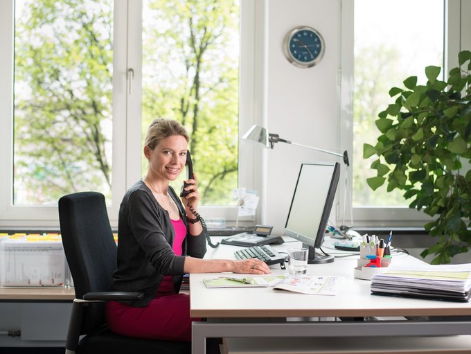 Auf dem Bild ist eine junge Frau abgebildet, die am Schreibtisch sitzt und telefoniert.